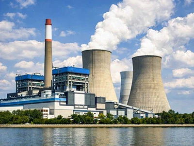 A vast power generation facility situated beside a serene body of water, with towering cooling structures and industrial machinery generating essential energy to meet growing demands.
