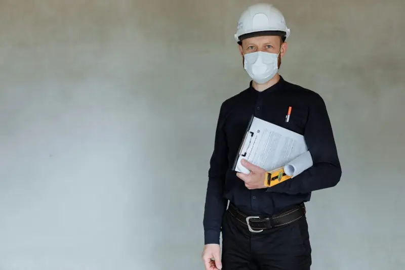 Construction worker wearing safety gear and holding documents during pandemic.